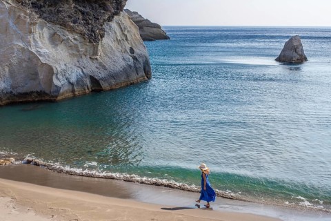 Unrecognizable woman in blue dress walking along beach Gerontas on island of Milos, Greece. The