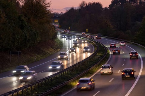 Evening scene on a motorway with heavy traffic, illuminated by headlights under a twilight sky,