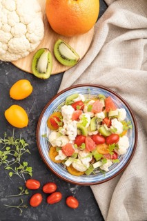 Vegetarian salad of cauliflower cabbage, kiwi, tomatoes, microgreen sprouts on black concrete