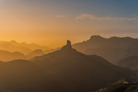 An enchanting sunset view of Roque Nublo standing distinct against a backdrop of layered mountain
