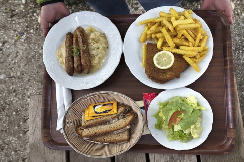 Sausages with sauerkraut and bread and cordon bleu with French fries served on a tray in a garden