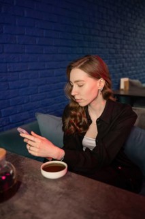 A woman sits in a cozy bar, engaged with her smartphone. Her tea sits on a table against a stylish