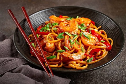 Udon stir-fry shrimp noodles with red bell pepper and green onion, served in a black bowl, with