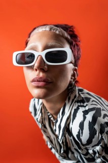 A bold fashion model wears a striking animal print outfit and oversized white sunglasses against a