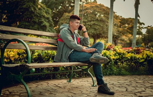 Man sitting on a bench calling on the phone, young man sitting on a bench with cell phone, close up