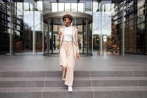 A fashionable black woman with a confident smile, wearing a beige outfit and sunglasses, walking