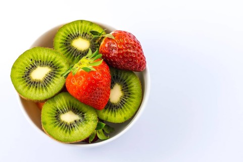 Sliced kiwis and strawberries in a white bowl with a white background