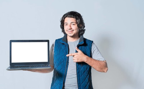 Smiling young man pointing at laptop screen isolated. Friendly guy pointing at a blank space on the