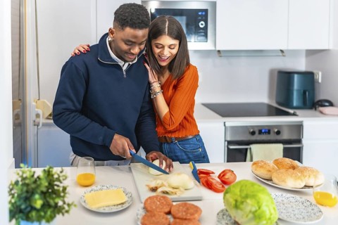 Young multiethnic couple preparing burgers together in their modern kitchen, enjoying their quality