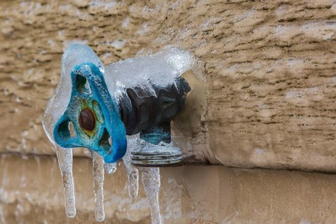 Close-up of outdoor utility brass water faucet with blue handle mounted through Canexel siding on