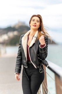 Fashionable woman in a leather jacket gazing at the scenic view from a pier, enjoying the coastal