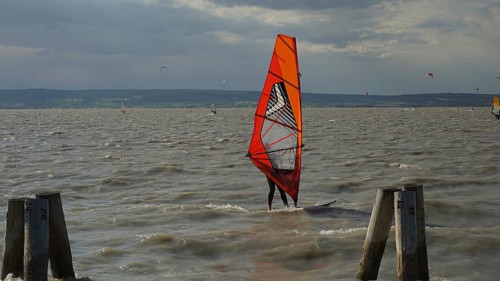 A windsurfer with a red sail stands out against the cloudy sky in the water, Lake Neusiedl, Austria