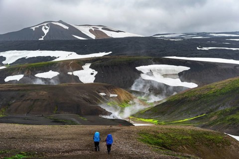Hikers in dramatic volcanic landscape with mountains and snow, volcanic steaming hot springs,