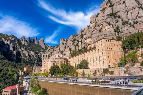 Tourists walking near the benedictine abbey, santa maria de montserrat, built into the mountainside