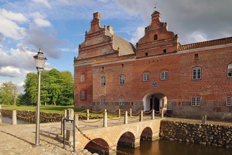 Historic brick castle with bridge over a moat on a cloudy day, Broholm, manor house route, Funen,