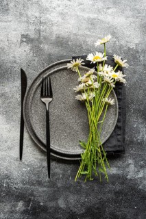 Top view of a daisy arrangement on rustic concrete with black cutlery and ceramic plates, creating