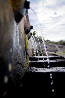 Close-up view captures water flowing through an old, moss-covered stone water channel, symbolizing