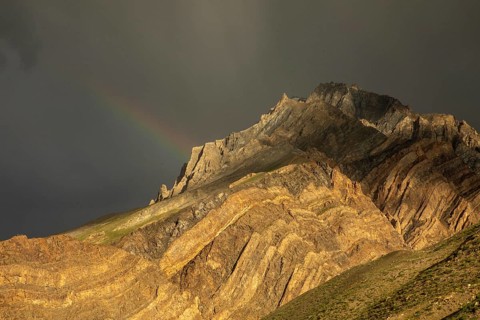 A breathtaking view of a rugged mountain in Spiti Valley, India, adorned with a delicate rainbow