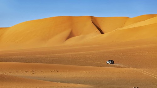 An off-road vehicle crosses a vast desert landscape under a bright blue sky, Off-road vehicle