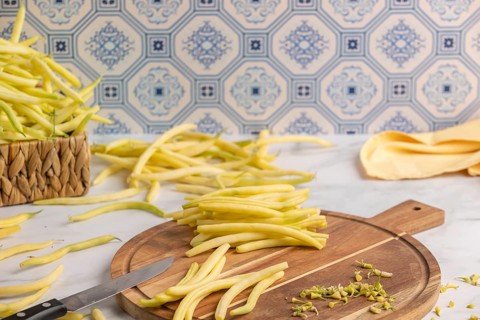 Sliced yellow beans on a wooden chopping board, whole beans in the background