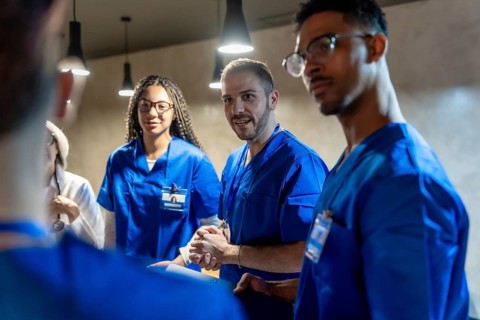 Multi ethnic medical team in blue scrubs and a physician in a white coat collaborating and