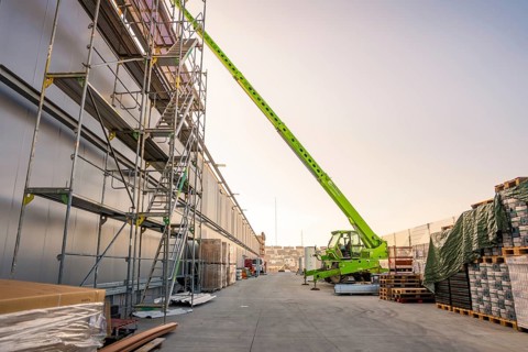 Construction site with tall crane and scaffolding, building materials are spread over a wide road,