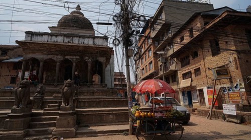 Street scene with a sales stand and a tangle of electrical cables in front of an old temple in