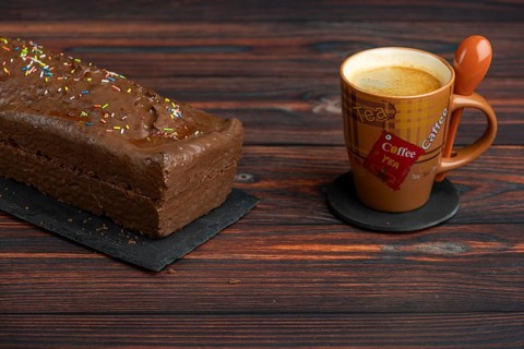 A chocolate cake next to a coffee cup on a wooden table