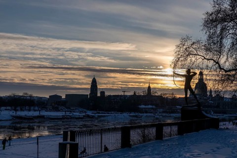 Bronze figure The archer in the snow, in the background the Elbe with drift ice and the old town