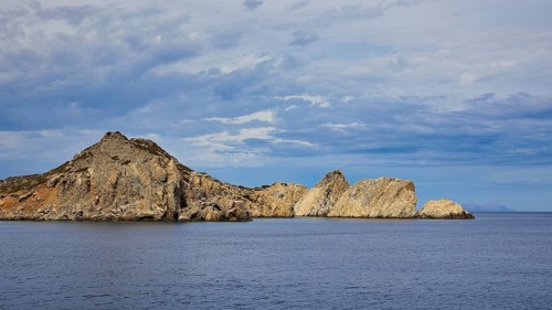 Barren rocks rise from the calm sea under a slightly cloudy sky, boat tour Saria, Saria Island,
