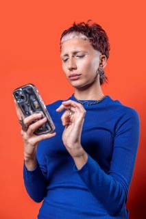 A stylish woman in a blue top looks at her smartphone against a bold orange backdrop. The scene