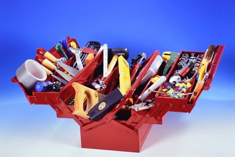 A red toolbox with tools, hammer, screwdriver, adhesive tape, folding rule, pliers, chisel, plane,