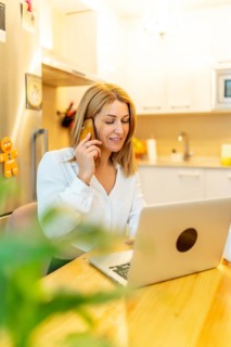 Vertical photo of a blonde businesswoman attending a call working from home sitting on a table next