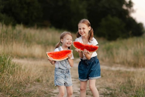 Two smiling children hold juicy watermelon slices in a sunlit field during summer. The scene