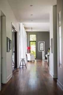 Main hallway with Qumaru wood floorboards leading to living room with white leather armchair, red