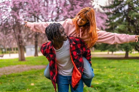 Interracial couple having fun together outdoors in a park during springtime with pink flowers