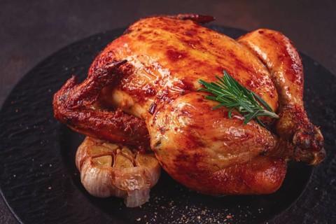 Baked chicken on a black dish with herbs and garlic, on a dark background, homemade, no people