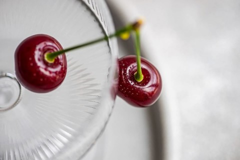 From above, a vibrant ripe cherry rests beautifully on a textured glass surface, highlighting its