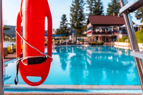 A red life preserver is hanging on a metal pole next to a pool. The scene is calm and peaceful,