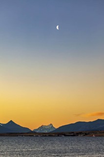 Half moon in the sky over a calm lake surrounded by mountains at dusk, sunset at the lake near