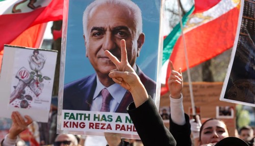 A demonstrator makes the peace sign in front of a poster by Prince Reza Pahlavi during an Iran