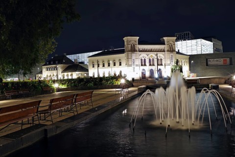 Historic building at night with illuminated fountain and benches in the foreground, old Ostbahnhof