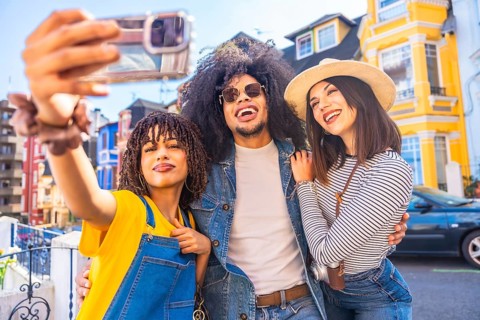 Three happy tourists taking a selfie with colorful buildings in the background, enjoying their