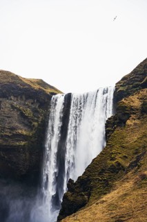 A stunning waterfall cascades down moss-covered cliffs in Iceland, creating a mesmerizing mist. The