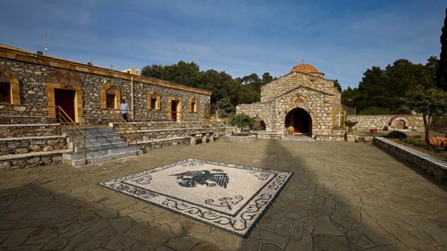 Stone building with church and mosaic in the courtyard under a blue sky, surrounded by trees, Thari