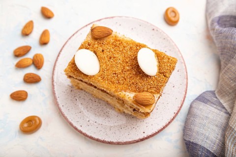 Honey cake with milk cream, caramel, almonds and a cup of coffee on a white concrete background and
