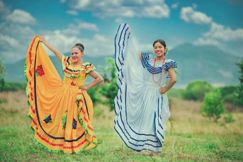 Portrait of two Hispanic girls wearing cultural folkloric costume in a field. Two happy Hispanic