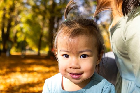 A young Asian child smiles brightly while enjoying a sunny day at a fall picnic. Surrounded by
