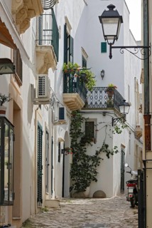 Narrow cobblestone alley in an old town with white facades, balconies with flowers and a parked