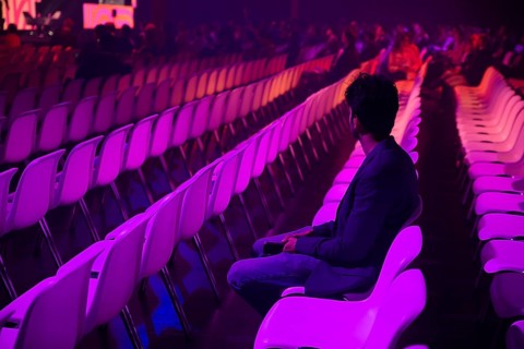 A indian man in a vast auditorium under dim purple lighting at a conference of AI in Amsterdam.